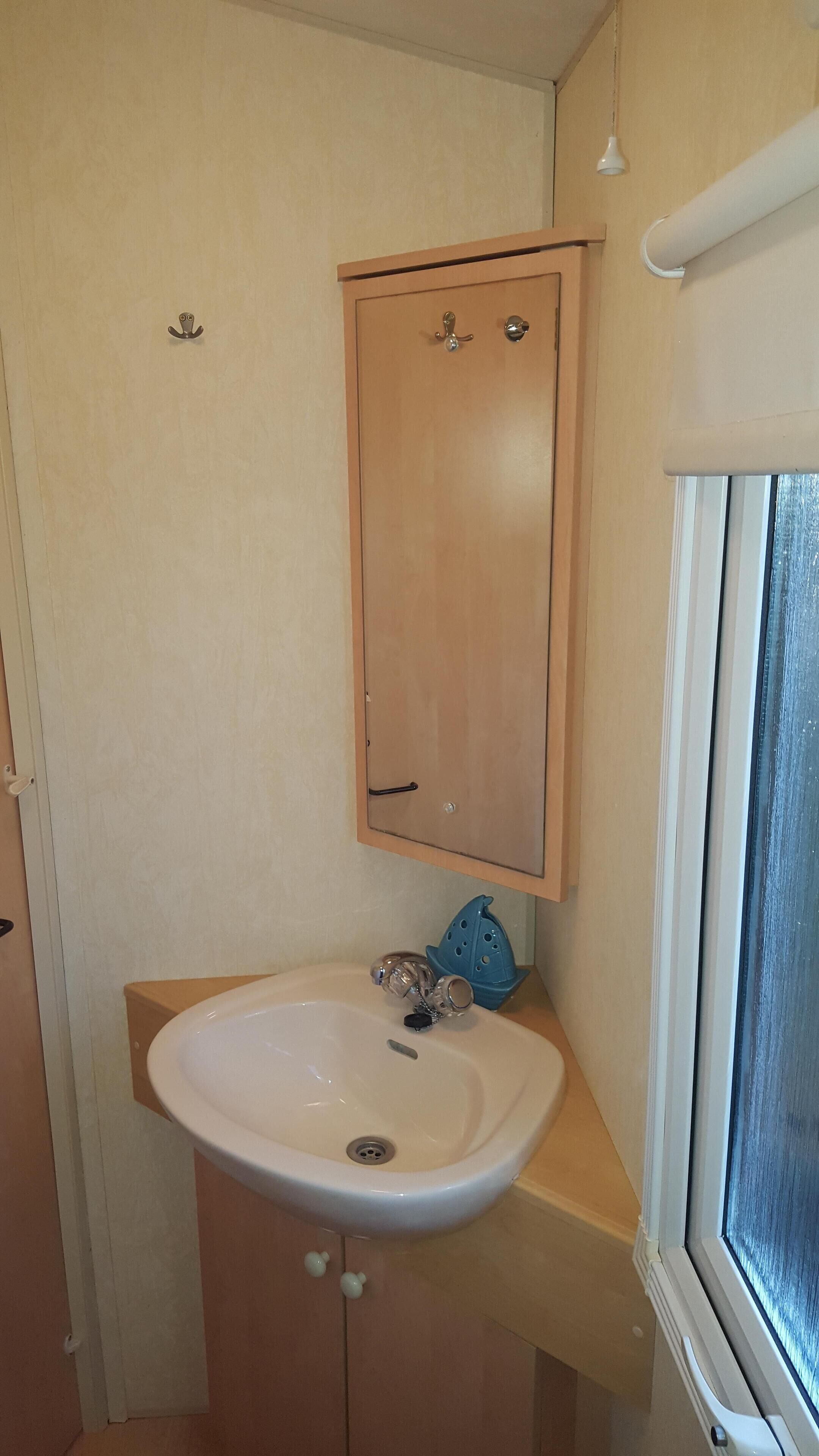 A compact bathroom with a wooden cabinet above a sink, a window on the right, and a door on the left.