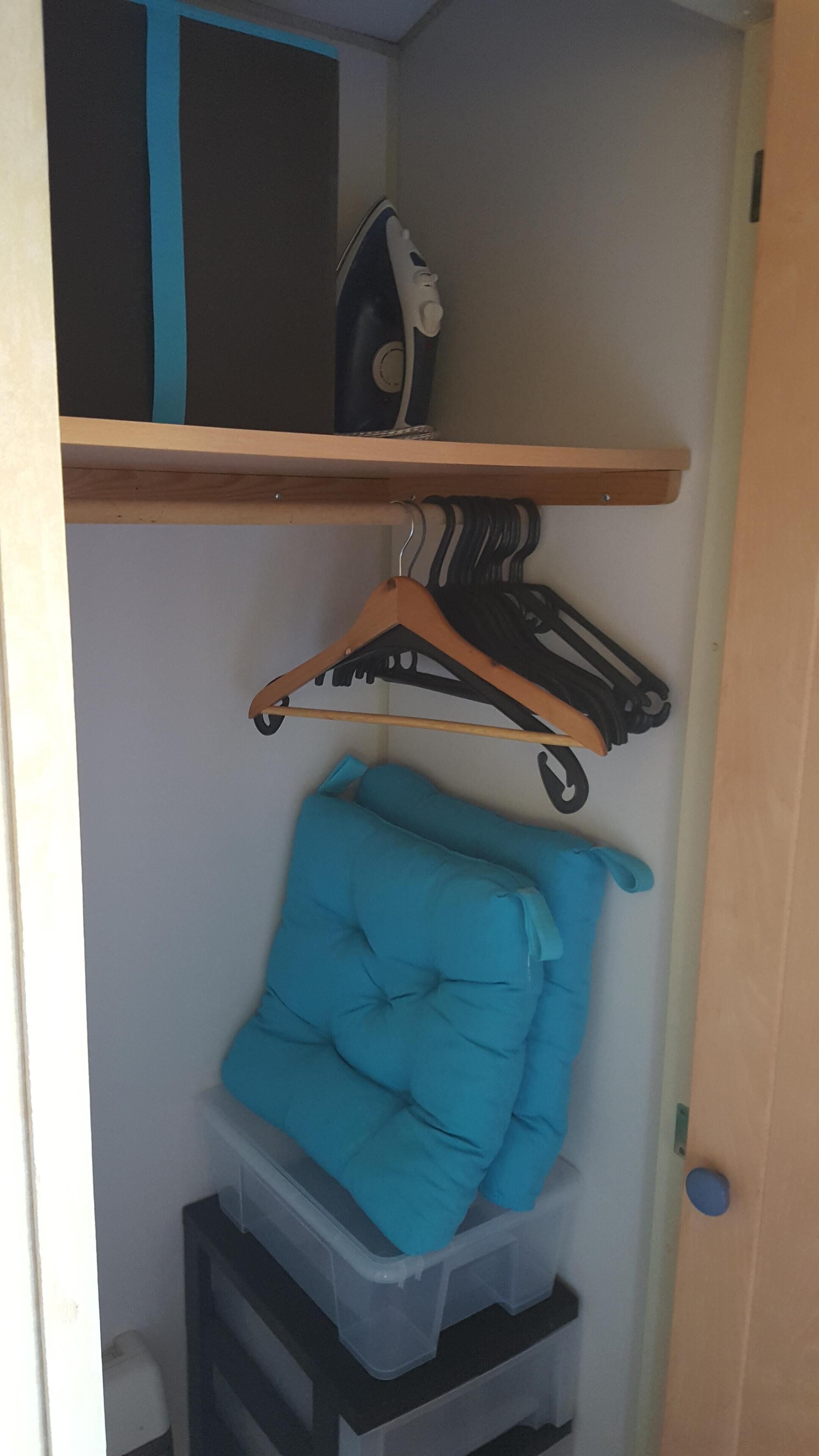 A closet with a hanging rack, a blue cushion, and a plastic storage bin.