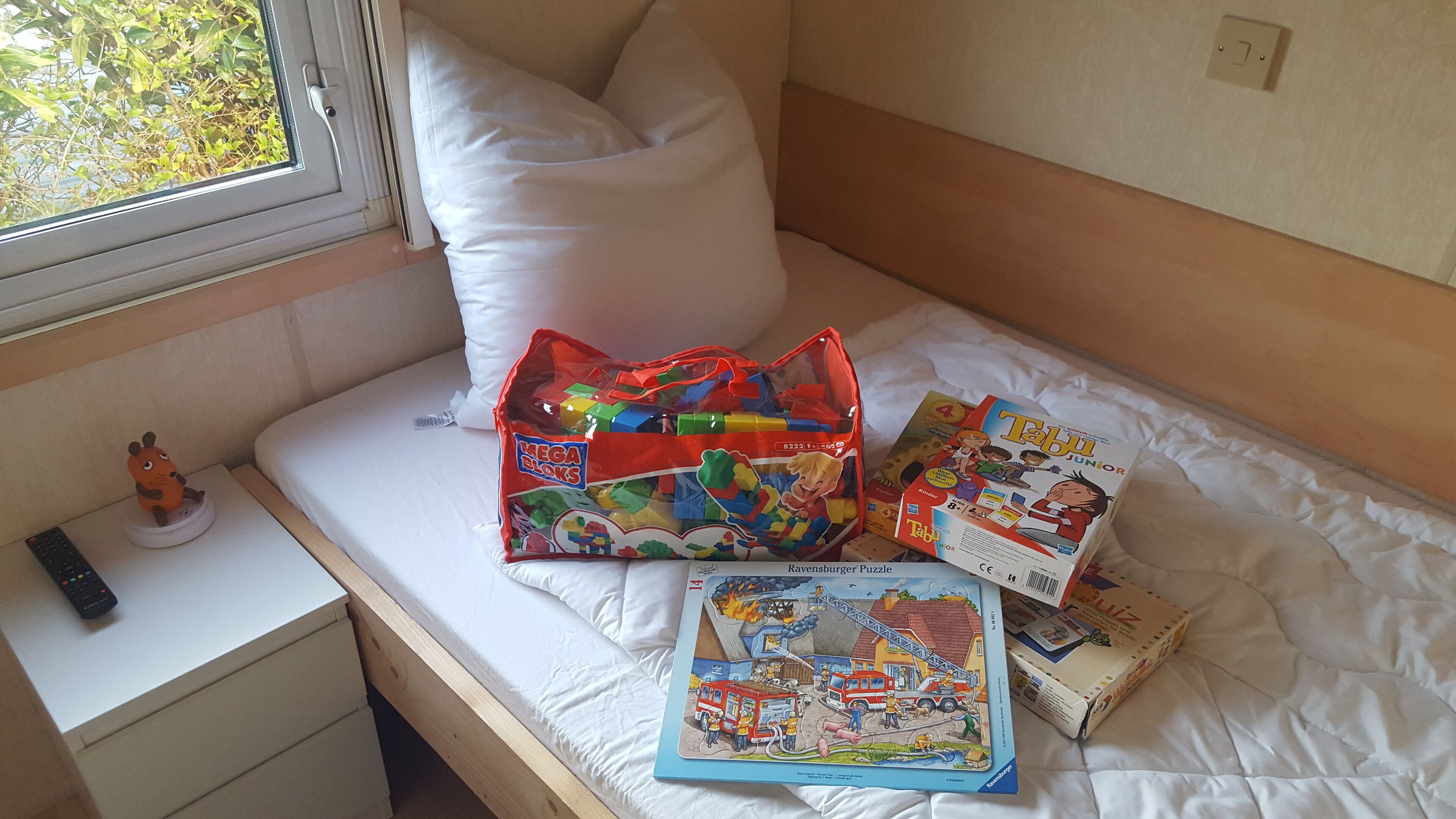 A bed with a white pillow, a bag of Mega Bloks, and children's books on a white mattress.