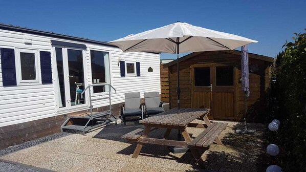 A mobile home with a patio area featuring a picnic table and an umbrella. - Modern chalet in Renesse at the 5* Beach & Camping Resort Julianahoeve (Renesse)