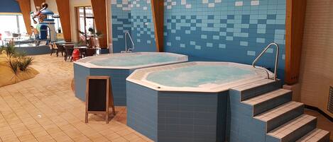 Duas banheiras de hidromassagem em área interna de piscina com azulejos e degraus de acesso.