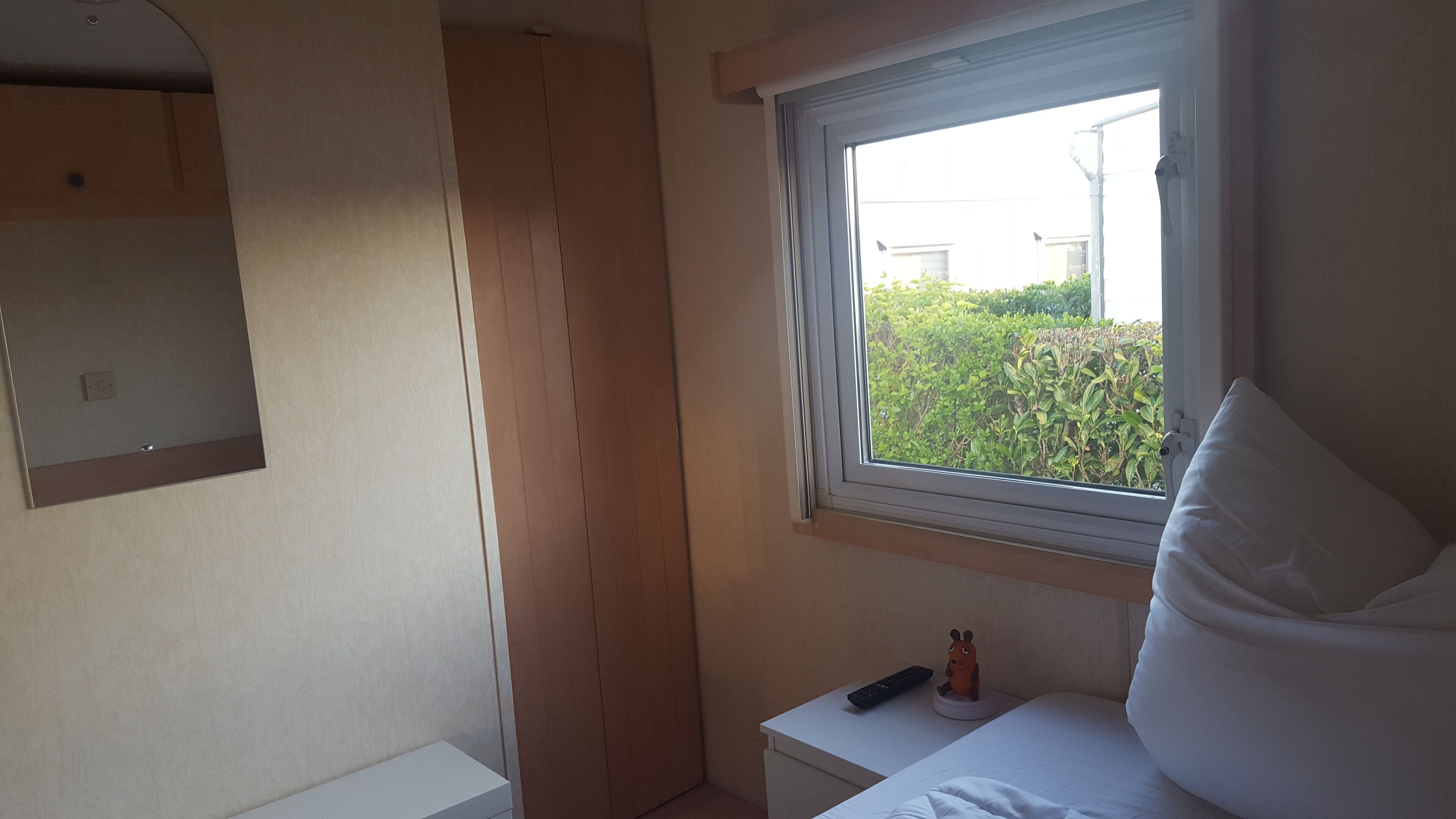 Una camera da letto con un letto singolo, un comodino con telecomando e una finestra vista sul verde.