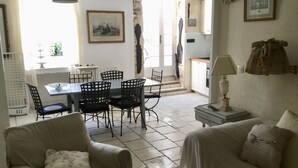 A living room with a sofa, a dining table with chairs, a lamp, and a view of the kitchen and outside.