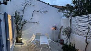 An outdoor patio with a white table and chairs, surrounded by potted plants and a white fence.