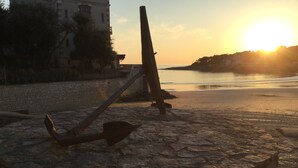 A stone pier with an anchor and a wooden post, overlooking a calm sea at sunset.