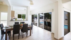 A spacious dining area with a table set for six, a kitchen area with a window, and a view of a swimming pool. - Villa Molly, Lovely 3BDR Protaras Villa with Pool, Close to Fig Tree Bay Beach (Protaras)