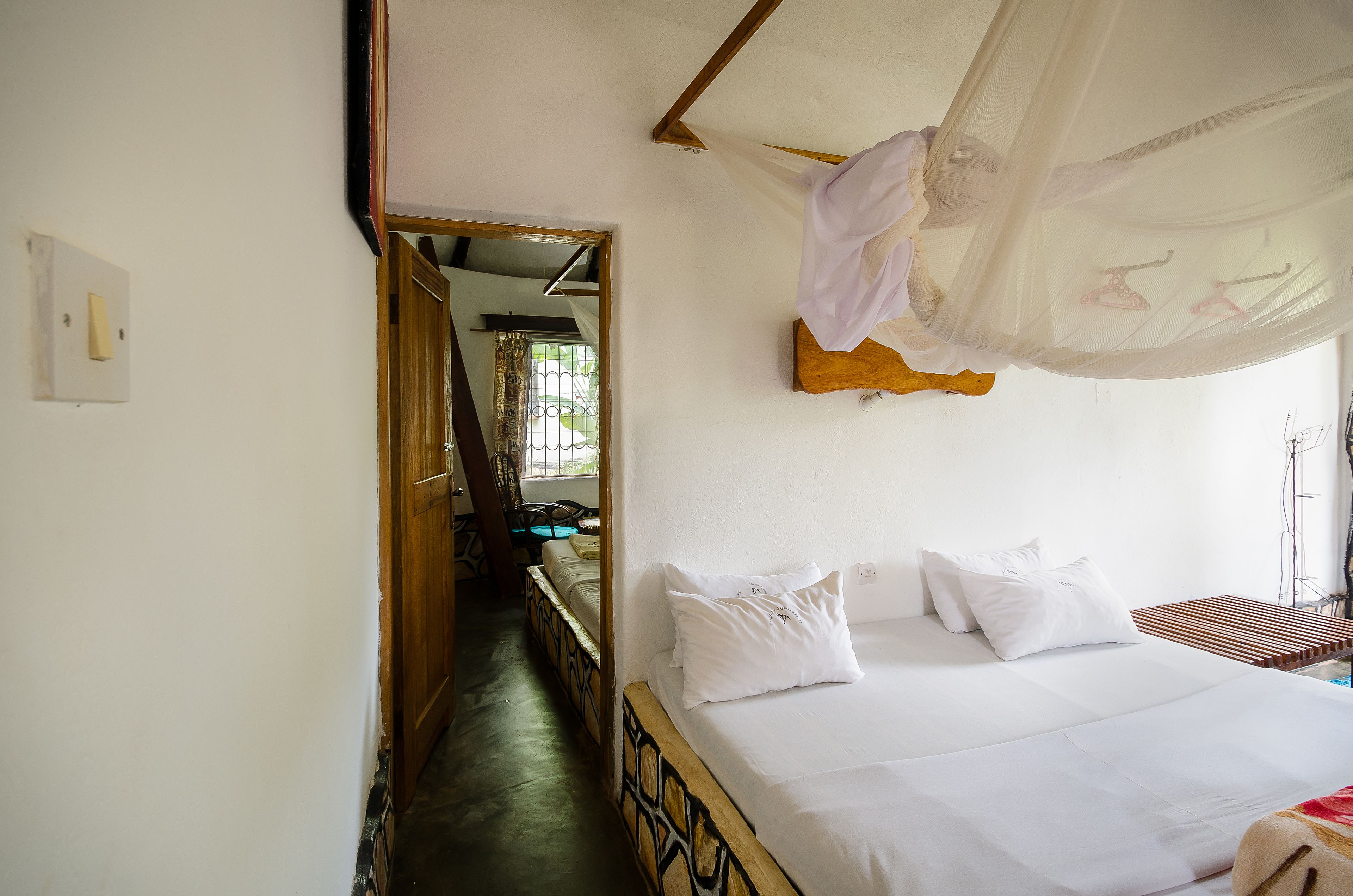 Un dormitorio con cama, ropa de cama blanca, cabecera de madera, mosquitero y vistas a una escalera y zona exterior.
