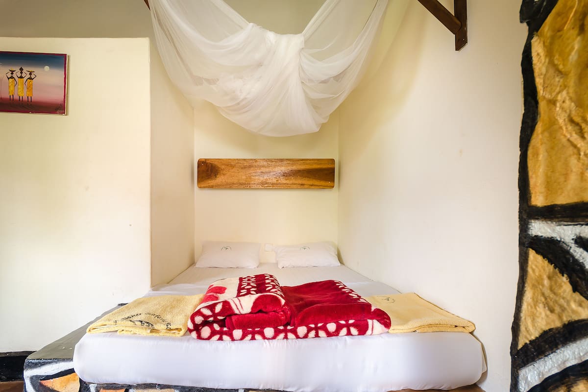 Een enkel bed met een witte matras, een deken met een rood-wit patroon en een wit hemeltje.