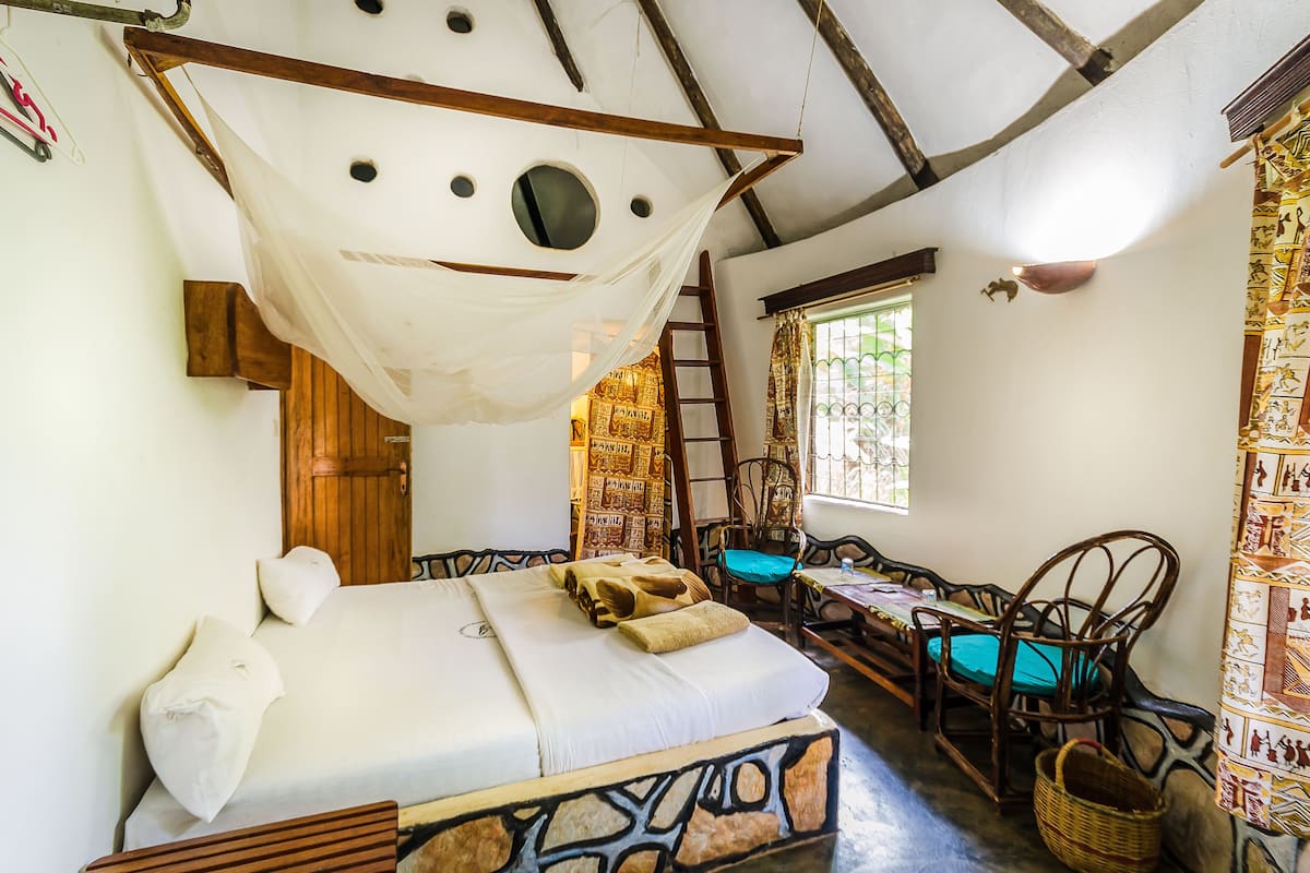 Een kamer met een bed, een houten trap, een raam met gordijnen en een gevlochten mand.