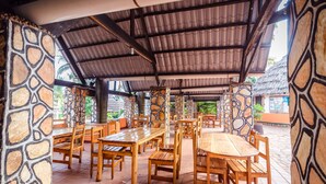 Un espace extérieur aménagé pour les repas, avec des tables et des chaises en bois, des murs en pierre et un sol carrelé.