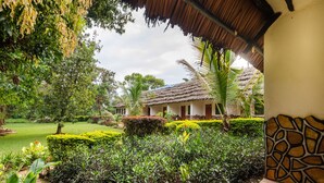 Une cour avec un bâtiment à toit de chaume, entourée de haies bien entretenues et de plantes tropicales.