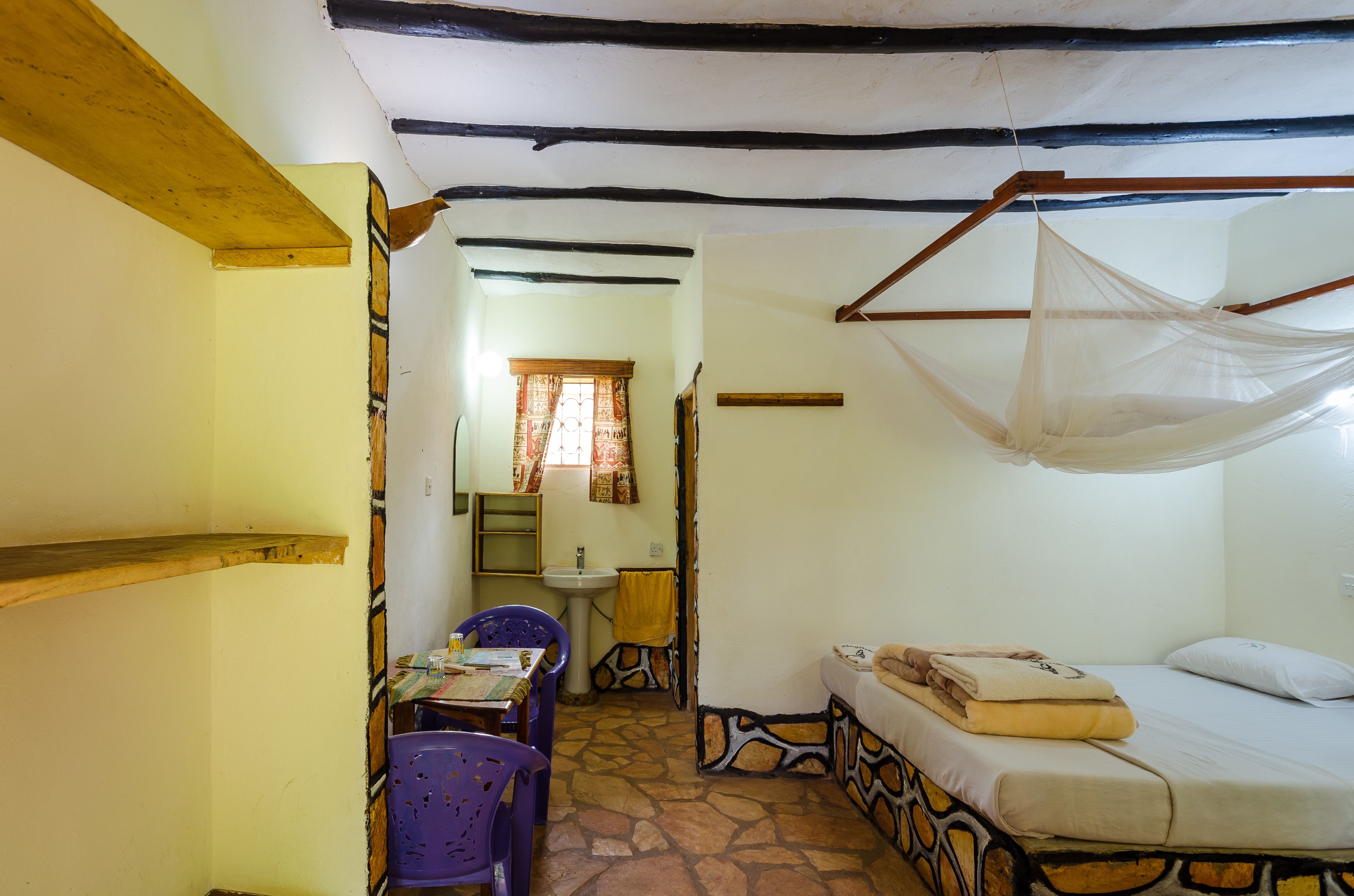 Una habitación con cama, mesa, silla, lavabo y ventana con cortinas.