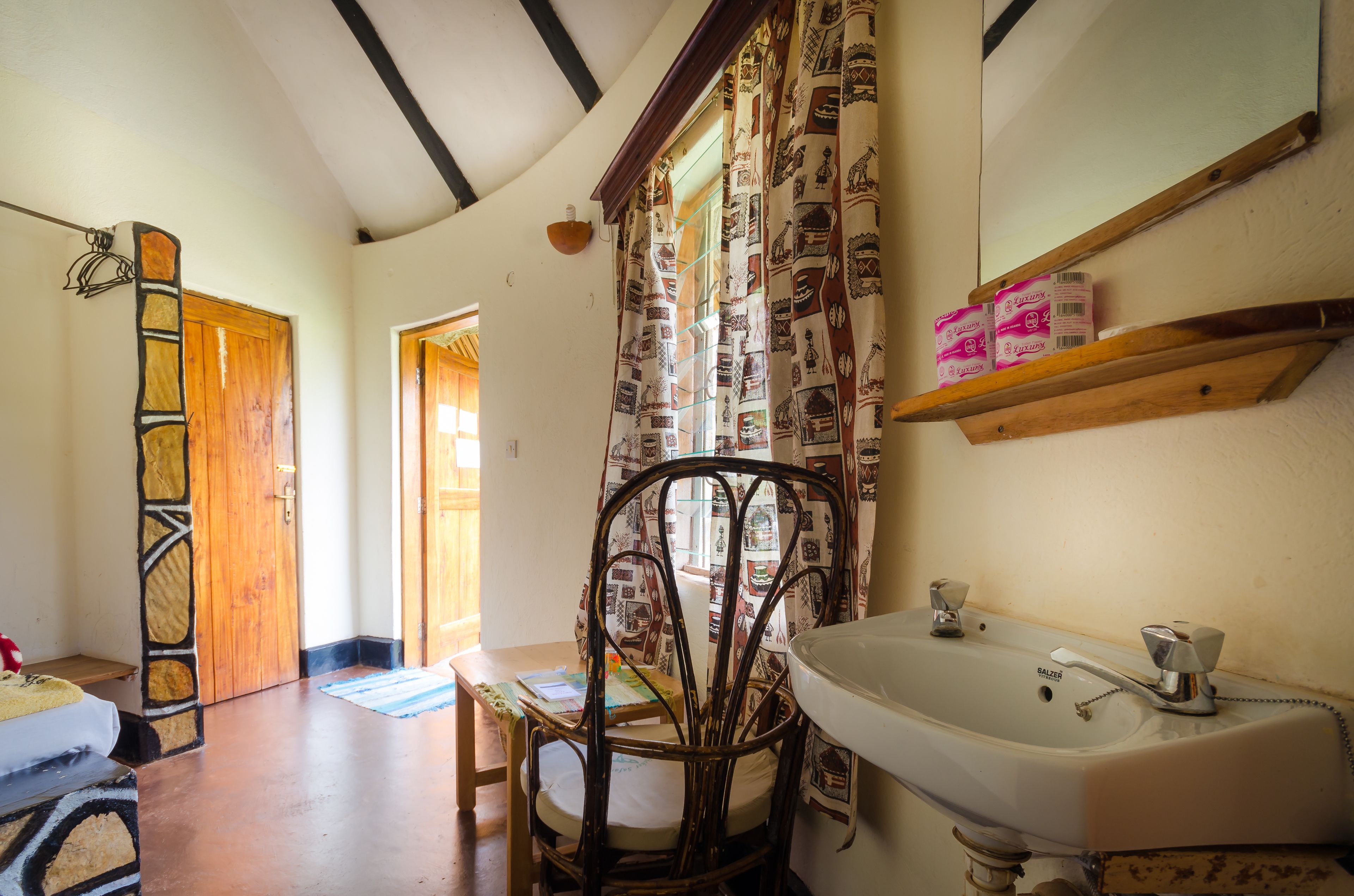 A bathroom with a white sink, wooden door, patterned curtains, and a mirror above the sink.