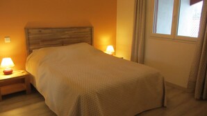 Ein ordentlich bezogenes Bett in einem Zimmer mit einem Holzkopfstück, zwei Nachttischlampen und einem mit Vorhängen versehenen Fenster.