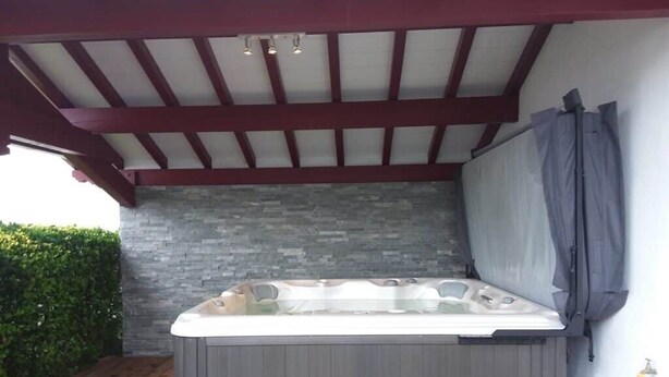 Ein Whirlpool unter einer Holzpergola mit einer Steinwand im Hintergrund.