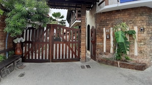 A gated entrance with a brick wall, a wooden gate, and a potted plant. - Melhores Suites (Arraial do Cabo)