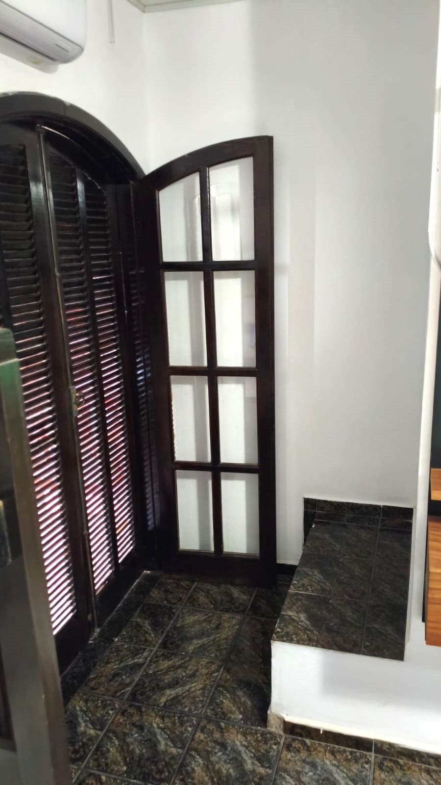 A corner room with a dark wooden door, a white wall, and a tiled floor.
