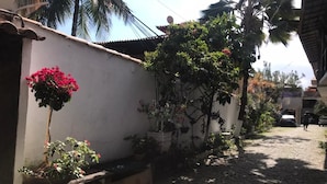 A cobblestone street with a white wall on one side, potted plants, and a palm tree. - Melhores Suites (Arraial do Cabo)