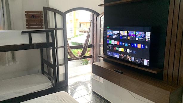 A room with bunk beds, a TV on a wooden stand, and a hammock. - Melhores Suites (Arraial do Cabo)