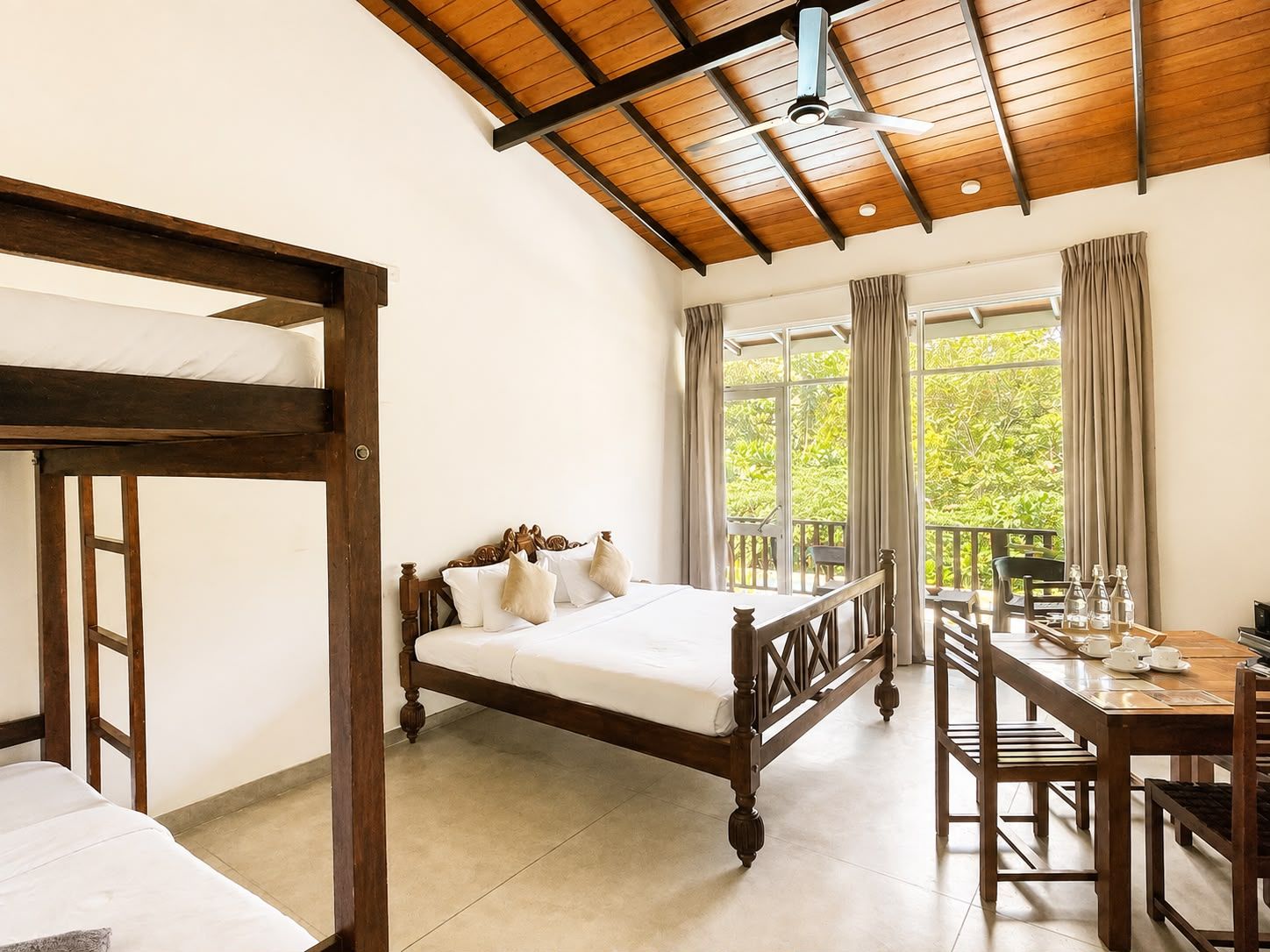 A room with a wooden bed, a desk with chairs, and large windows.