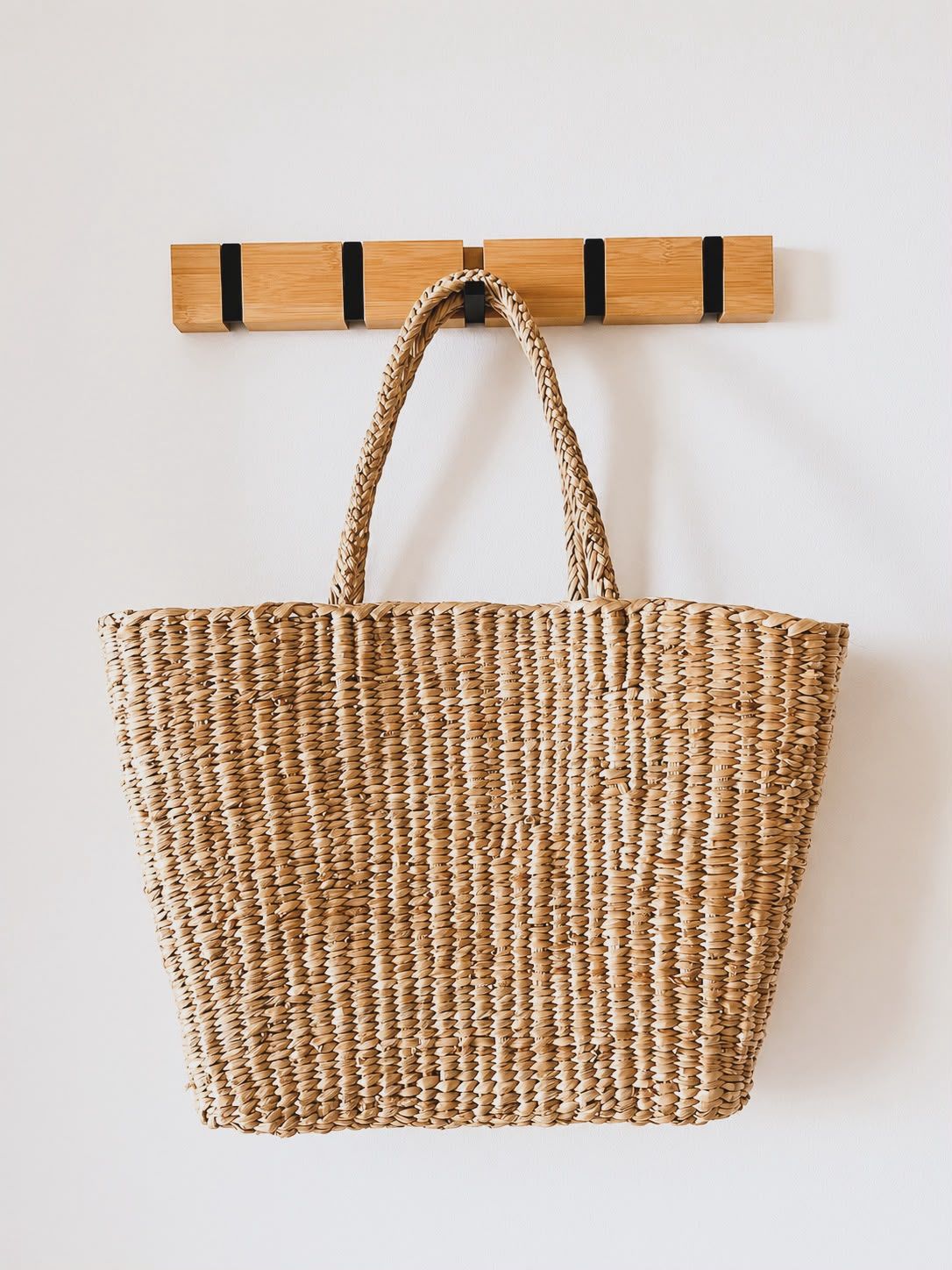 A woven tote bag hanging on a wooden rack.