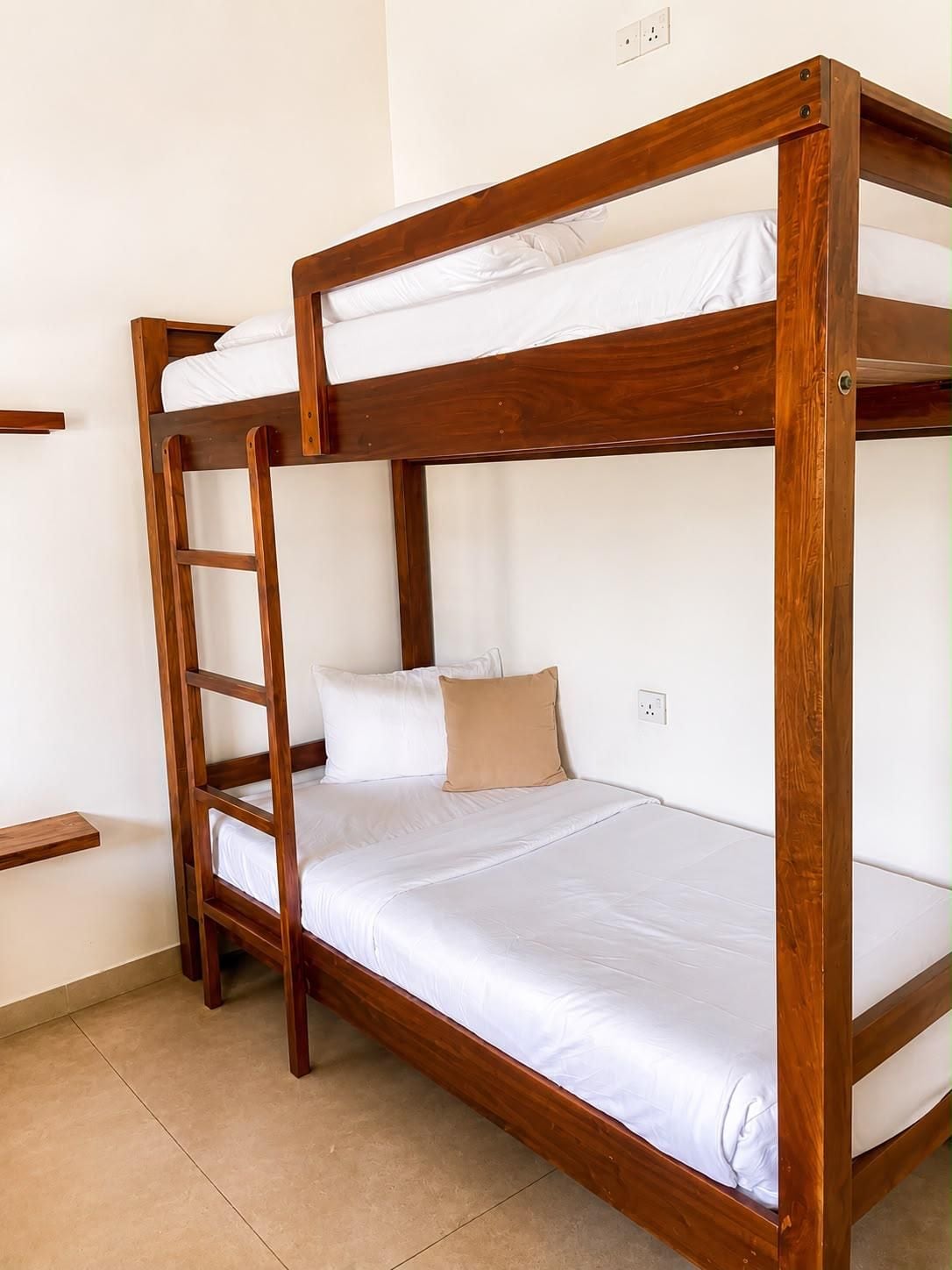 Un letto a castello con struttura in legno, biancheria bianca e un cuscino color beige.