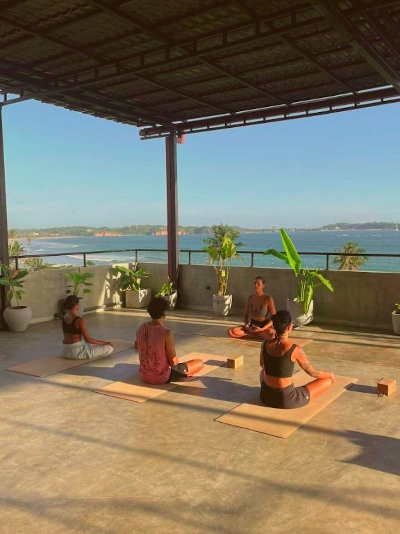 Eine Gruppe von Menschen meditiert auf einem Dach mit Blick auf das Meer.