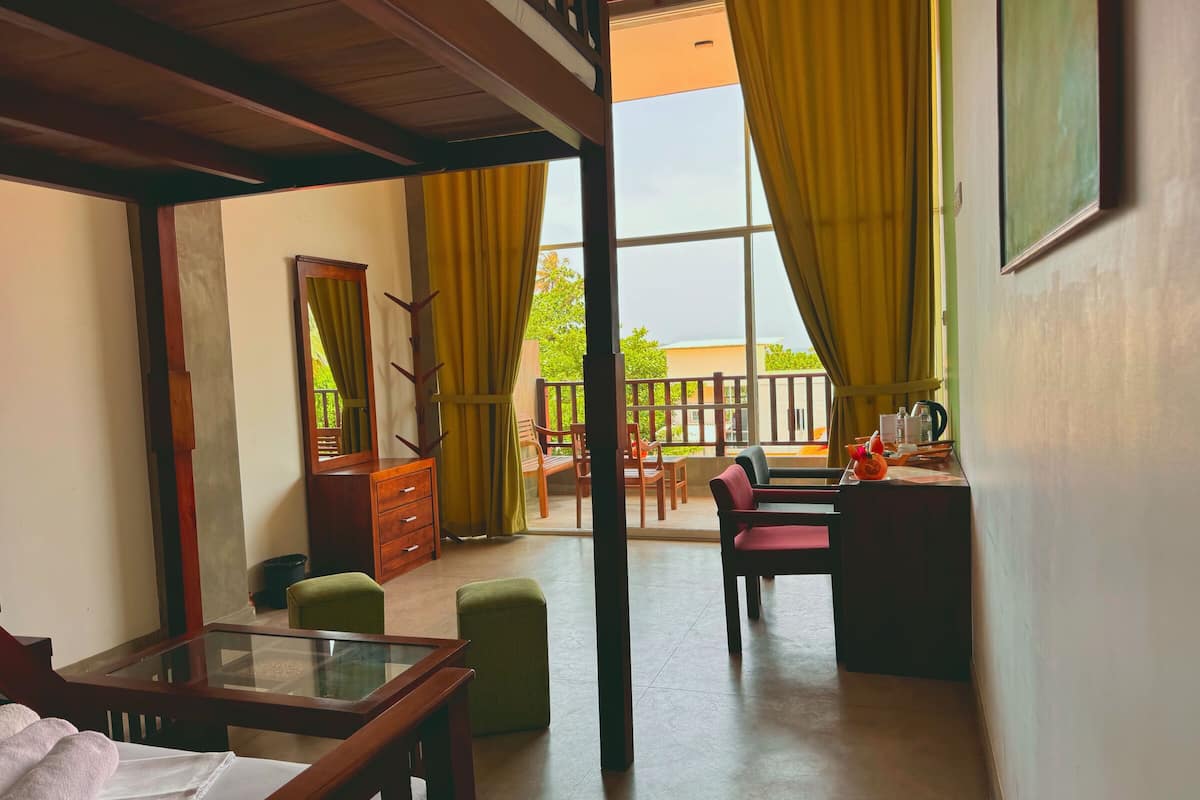 A room with a bed, a desk, a chair, a dresser, and a balcony with chairs.