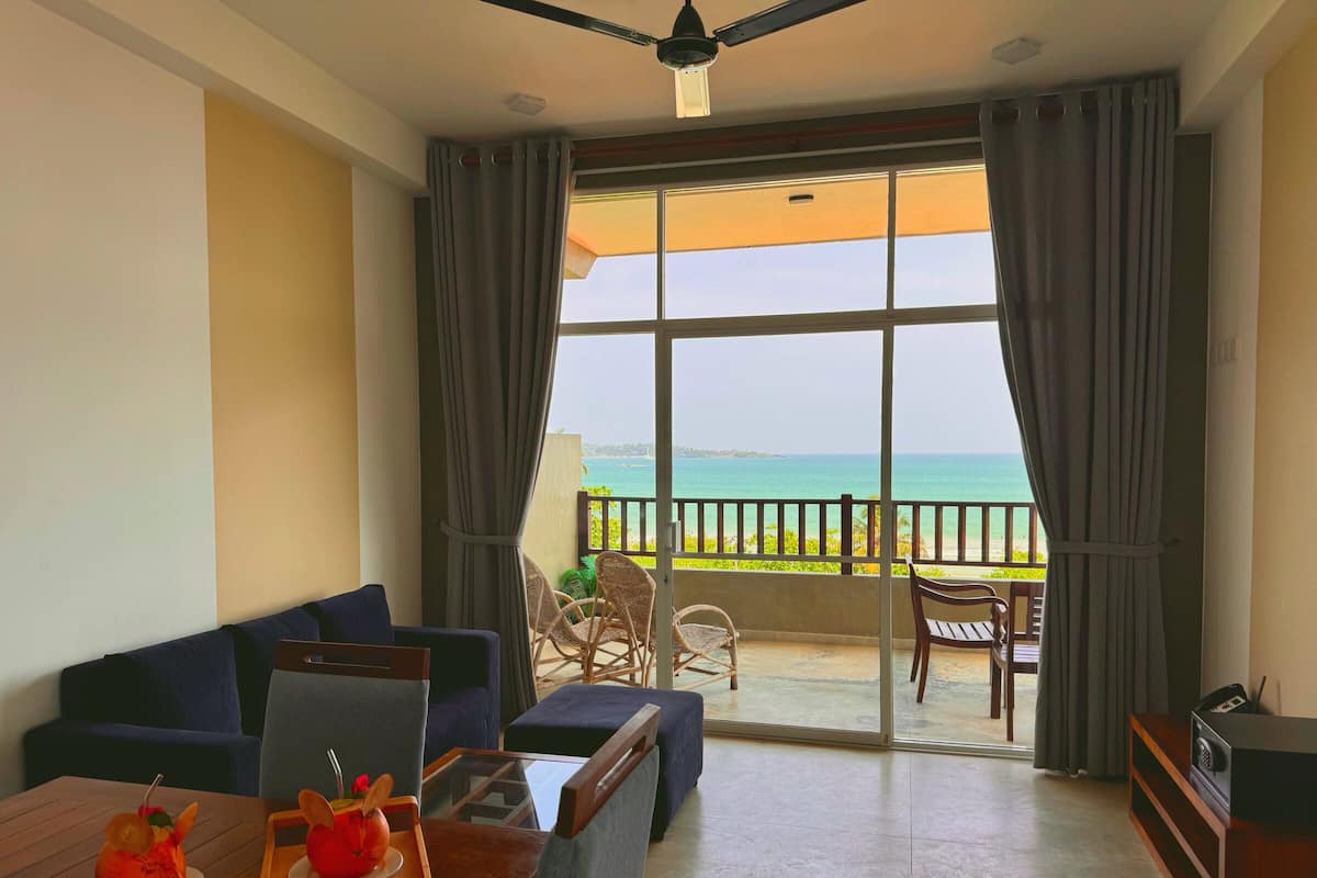 A room with a balcony, a sofa, a dining table with a tray of food, and a television.