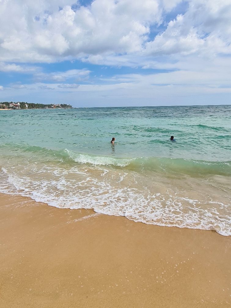 A beach with clear water, a sandy shore, and a distant shoreline with buildings.