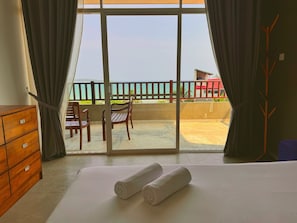 A room with a bed, two wooden chairs, a wooden dresser, and a balcony with a view of the sea. - Casa Samaya, Boutique Beachfront Hotel in Weligama (Weligama)