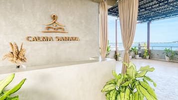 A reception area with a sign reading 'CALMA SAMAYA' and a view of the sea through large windows.
