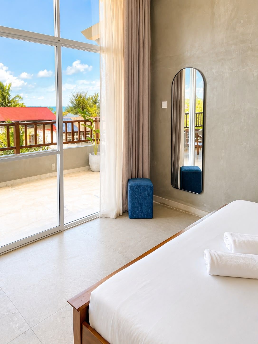Una habitación de hotel con un ventanal grande, una cama, un taburete pequeño y un espejo.