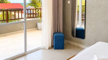 Una habitación de hotel con un ventanal grande, una cama, un taburete pequeño y un espejo.