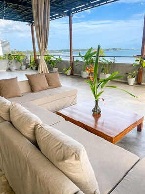A modern outdoor seating area with a sofa and a wooden coffee table, surrounded by potted plants and overlooking a body of water. - Casa Samaya, Boutique Beachfront Hotel in Weligama (Weligama)