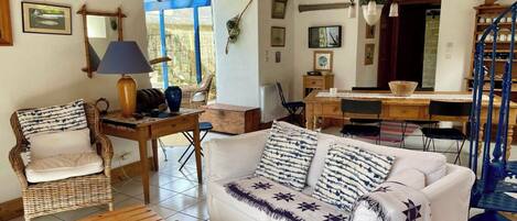 Un salon chaleureux avec un canapé blanc, un fauteuil en osier, une table basse en bois et une table à manger avec des chaises.