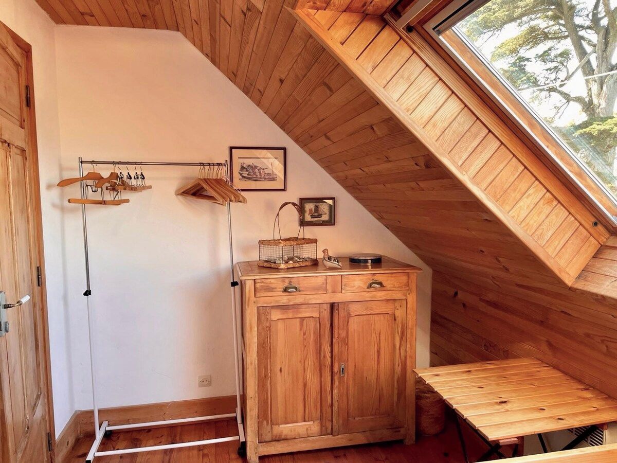 A wooden cabinet with drawers and a small table, a coat rack with hangers, and a picture on the wall.