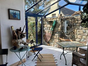 A conservatory with stone walls, a glass ceiling, and a rustic interior design including a table, chairs, and a decorative wall piece. - Idyllic house in Trébéron close to the sea B0018 (Crozon)