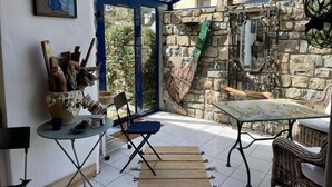 A sunlit patio with a glass enclosure, stone walls, rustic furniture, and a painting on the wall. - In the village Trébéron, Crozon peninsula,  (Crozon)