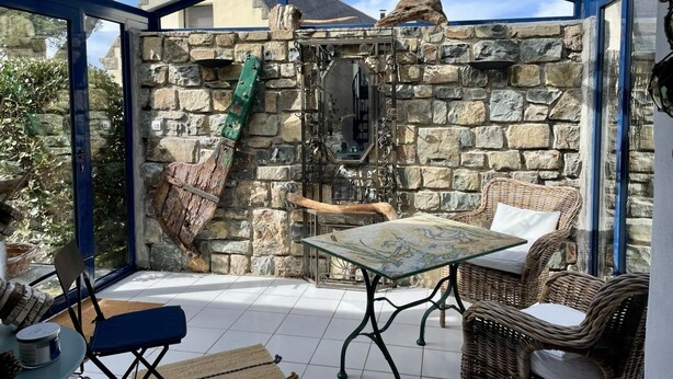 A conservatory with stone walls, a glass ceiling, wicker furniture, and a table with a decorative top. - In the village Trébéron, Crozon peninsula,  (Crozon)