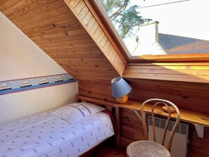A small, cozy room with a sloped ceiling, a single bed with a patterned bedspread, a wooden chair, and a table with a lamp. - Idyllic house in Trébéron close to the sea B0018 (Crozon)