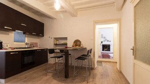 A modern kitchen with dark cabinets, a central island with chairs, and a dining table. - Il Cuore di Chiusi - House in the historic center (Unknown)