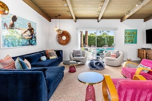 Uma sala de estar com um sofá azul, uma mesa de centro redonda e uma poltrona rosa.
