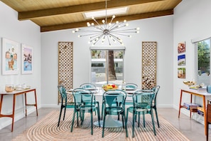 A dining area with a round table, teal chairs, a patterned rug, and a modern chandelier.