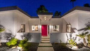 A modern house with a red door, white walls, and a covered entrance.