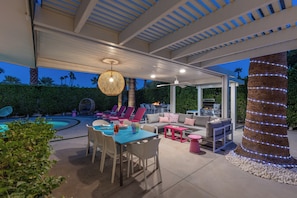 An outdoor patio with a pool, seating area, and a grill.