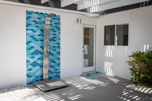 A modern outdoor shower area with a tiled wall, a metal showerhead, and a step leading to a door. - Fiesta in the Sun - Luxe Palm Springs Oasis (Palm Springs)