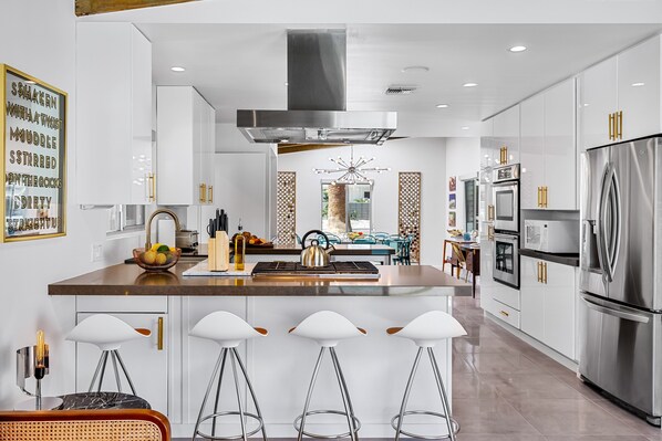 A modern kitchen with a central island, stainless steel appliances, and bar stools. - Fiesta in the Sun - Luxe Palm Springs Oasis (Palm Springs)