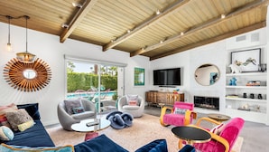 A modern living room with a pool view, a fireplace, and a TV.