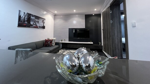 Ein modernes Wohnzimmer mit einer Couch, einer Glasschale auf dem Tisch und einem flachbildfernseher an der Wand.
